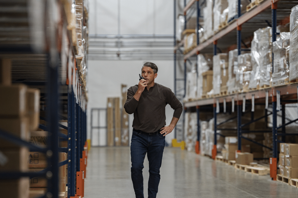 Medewerker met portofoon in een magazijngang tussen hoge stellingen